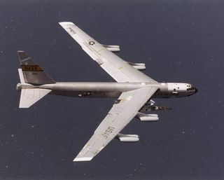 The NASA X-43A hypersonic research vehicle and its Pegasus booster rocket can be seen mounted beneath the wing of their B-52 mothership as it flies above the ocean.