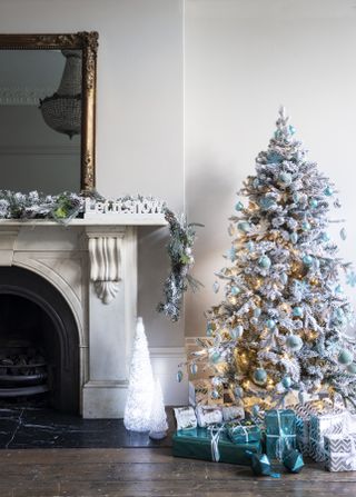 white frosted Christmas tree with teal blue decorations, garland on mantle and fireplace