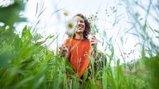 A smiling woman picks flowers in a green field.