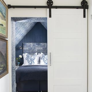 White sliding door with blue abstract wallpaper, blue bedding and white pillows