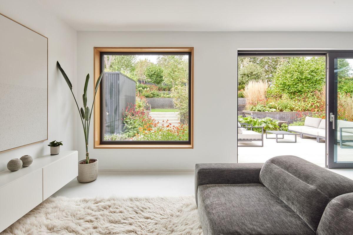 A large square window in a minimalistic livingroom with views of a green garden beyond