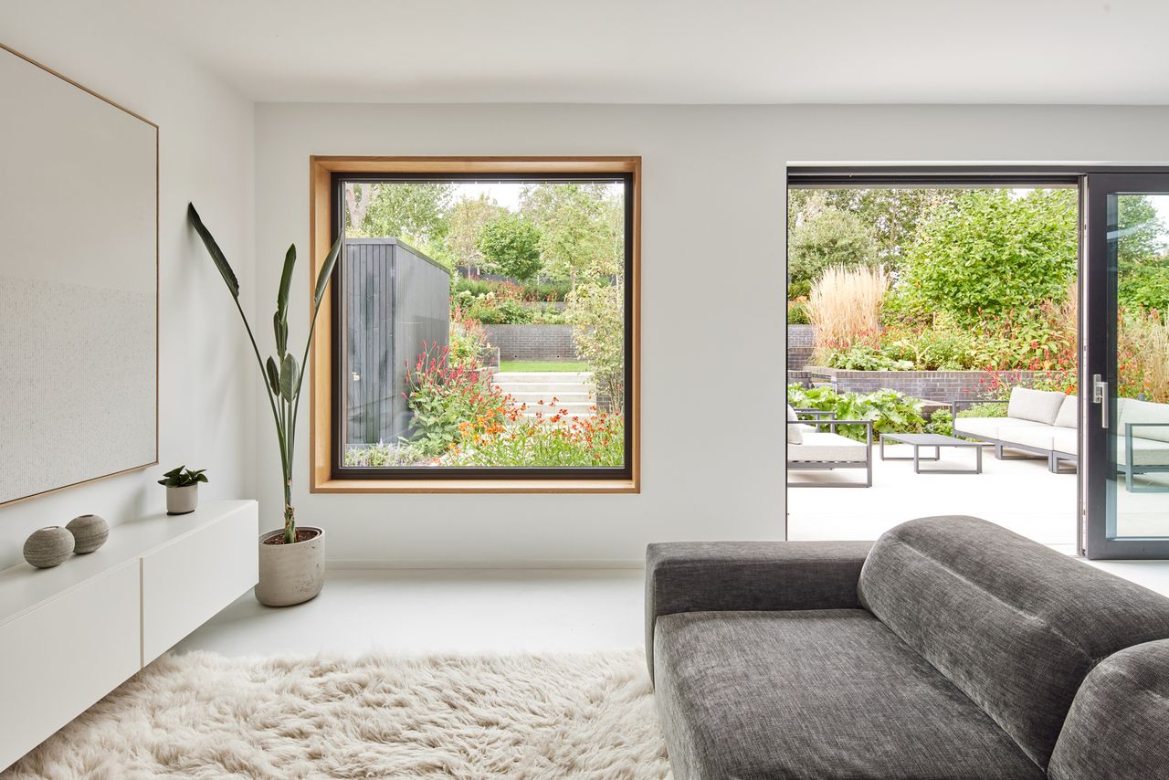 A large square window in a minimalistic livingroom with views of a green garden beyond