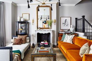 white living room with orange sofa and big gold mirror above the fireplace