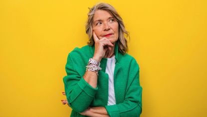 Thoughtful mature woman in green jacket in front of yellow wall 