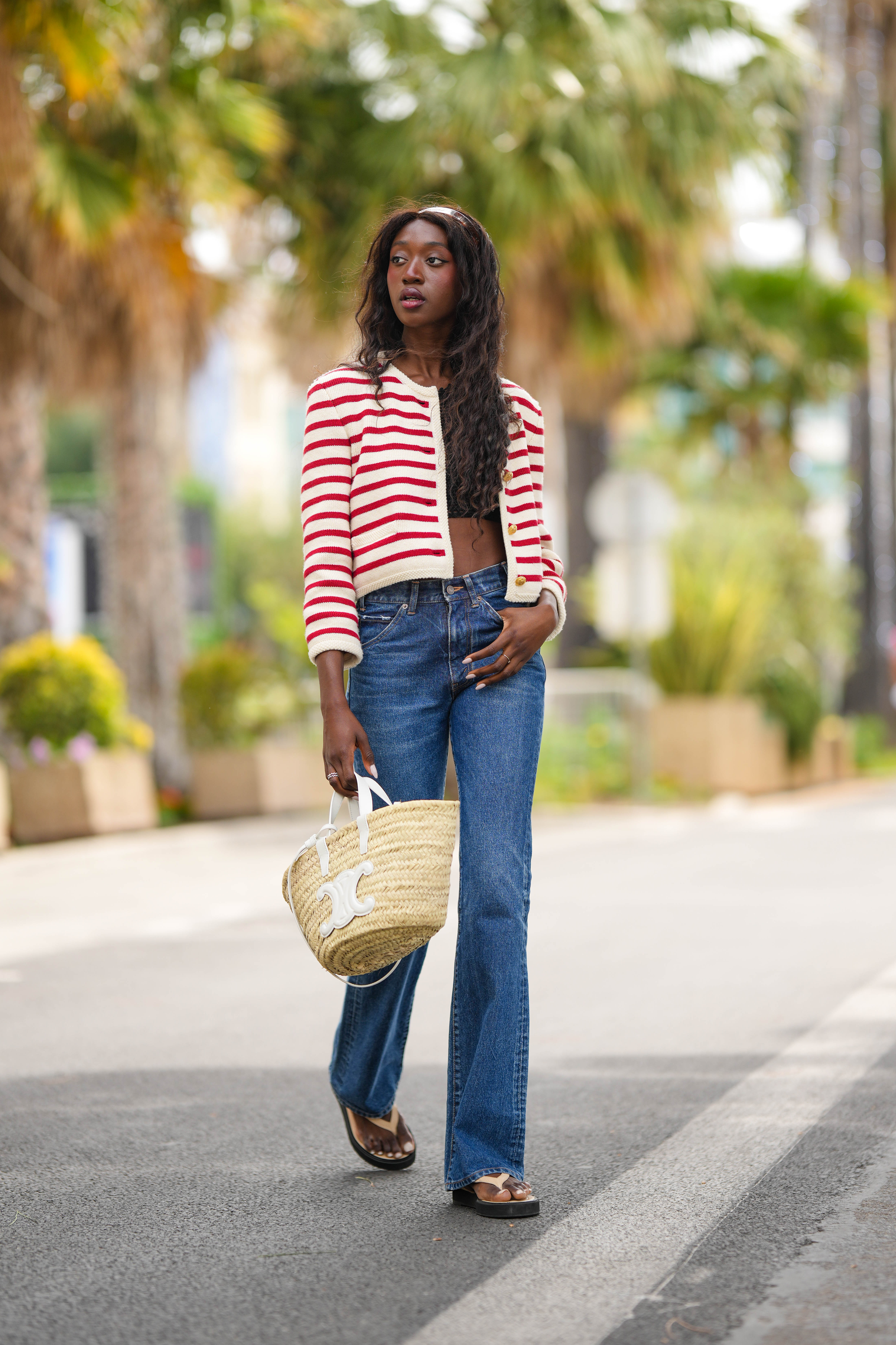 Emmanuelle Koffi wears a Celine red and white stripe jacket, a black crop top, blue jeans, and flip-flops.