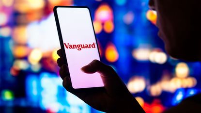 A hand holds a smartphone with the Vanguard app loading