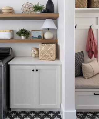 A laundry room with white cabinets, tiled floors, and wooden open shelving