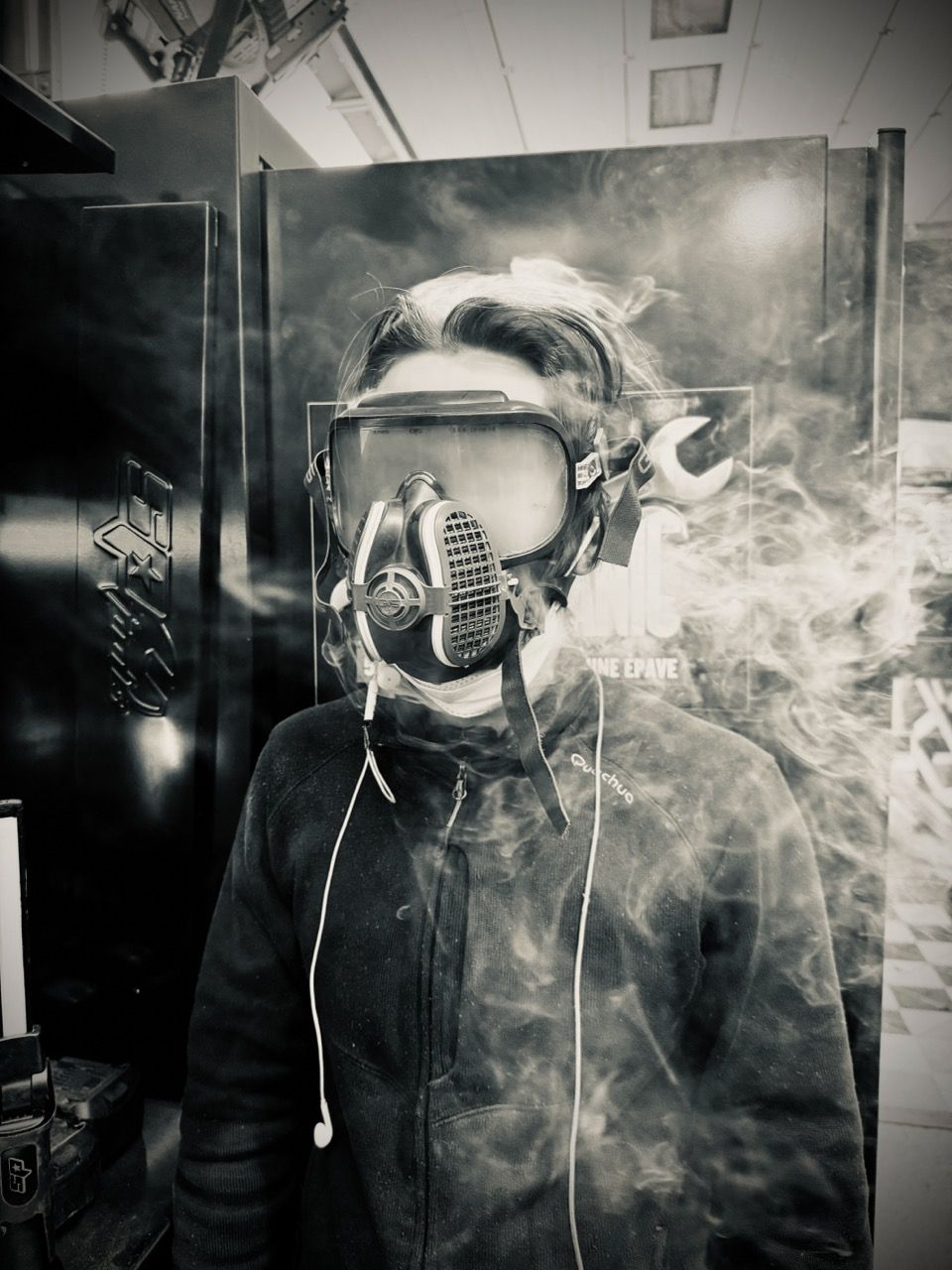 Monochrome photograph of a young person wearing a gas mask. A large amount of vapor is issuing from behind it, obscuring their face