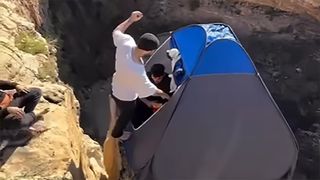Man jumping into tent on cliff edge
