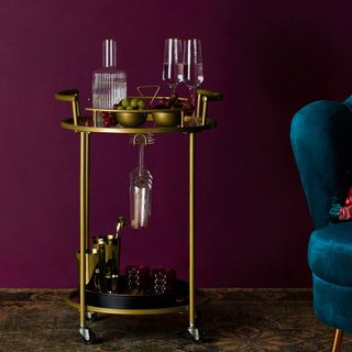Primark bar cart, two levels with glasses and alcohol on in front of purple wall