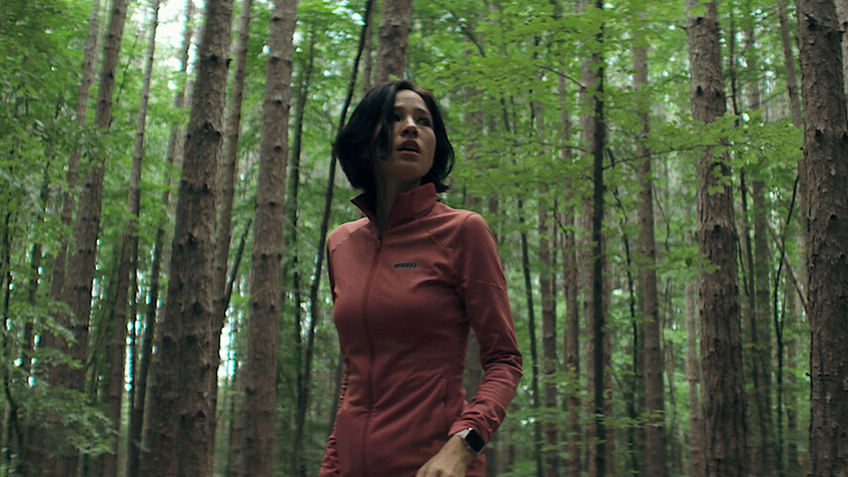 A girl stands in the middle of a forest wearing running gear