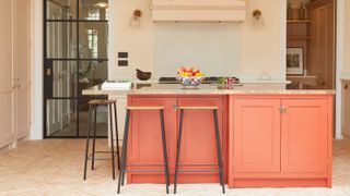 orange kitchen island unit with two black and wooden seated stools