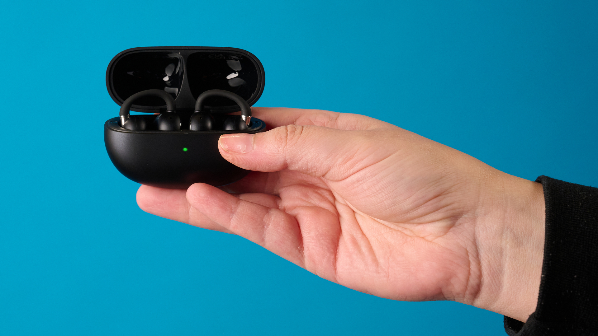 Han holding the EarFun Clip 2 in black photographed in front of a blue background