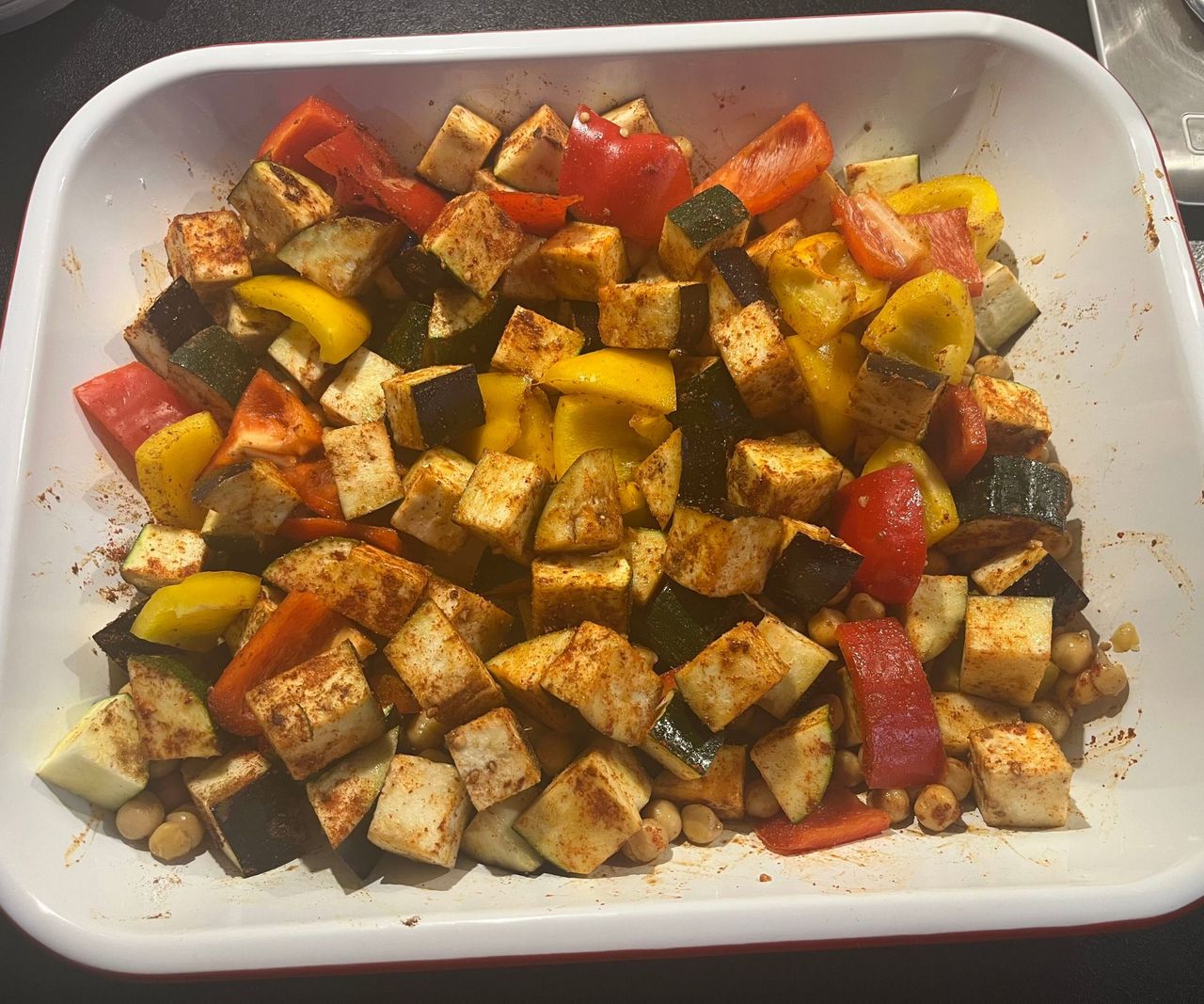 A white enamel dish with a red rim, with a selection of vegetables tossed in spices inside.