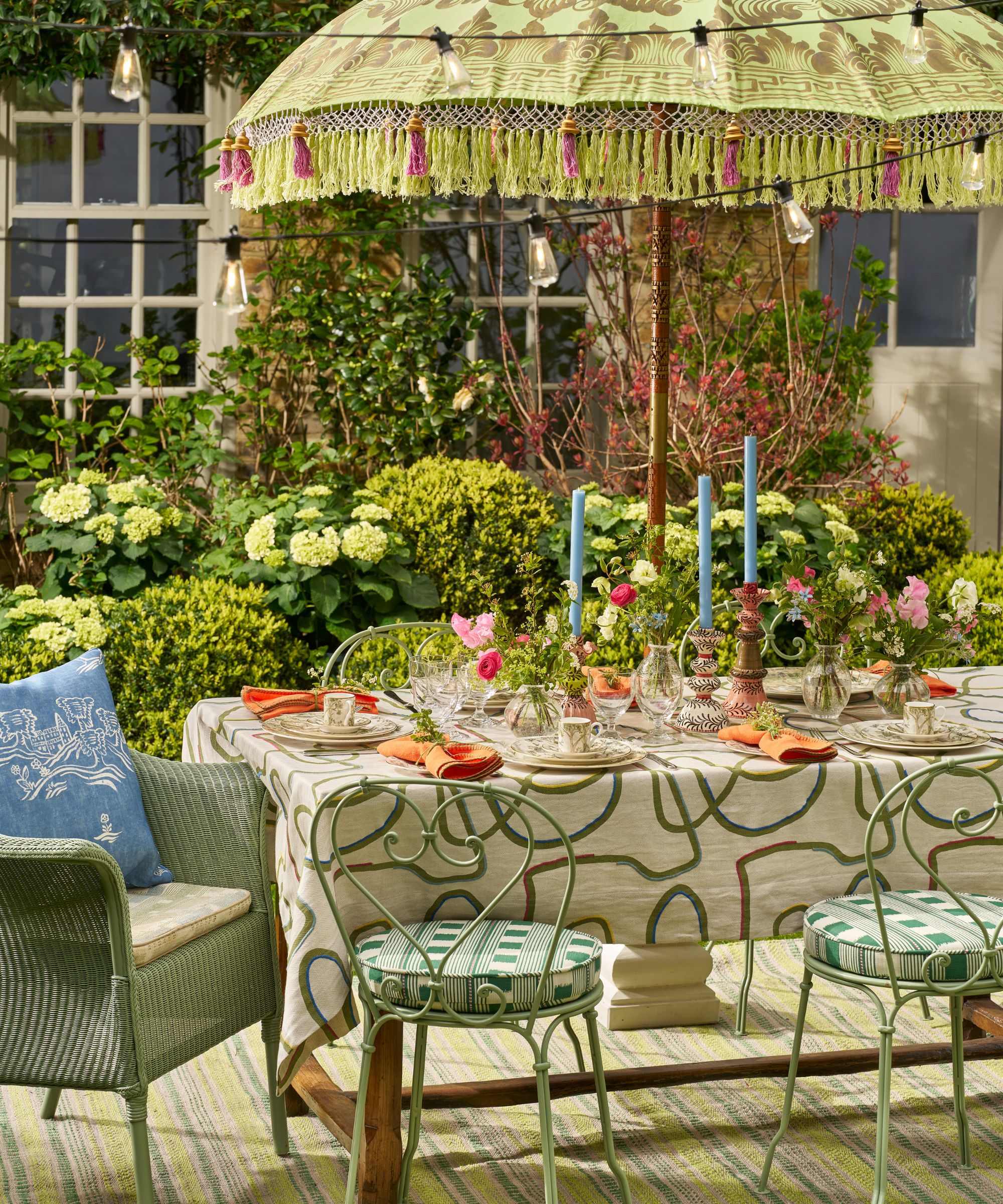 green themed garden party tablescape with heart shaped iron chairs, a printed patio umbrella, and an eclectic table setting