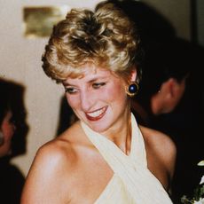 Princess Diana smiles while wearing a pale yellow halter dress and large blue earrings