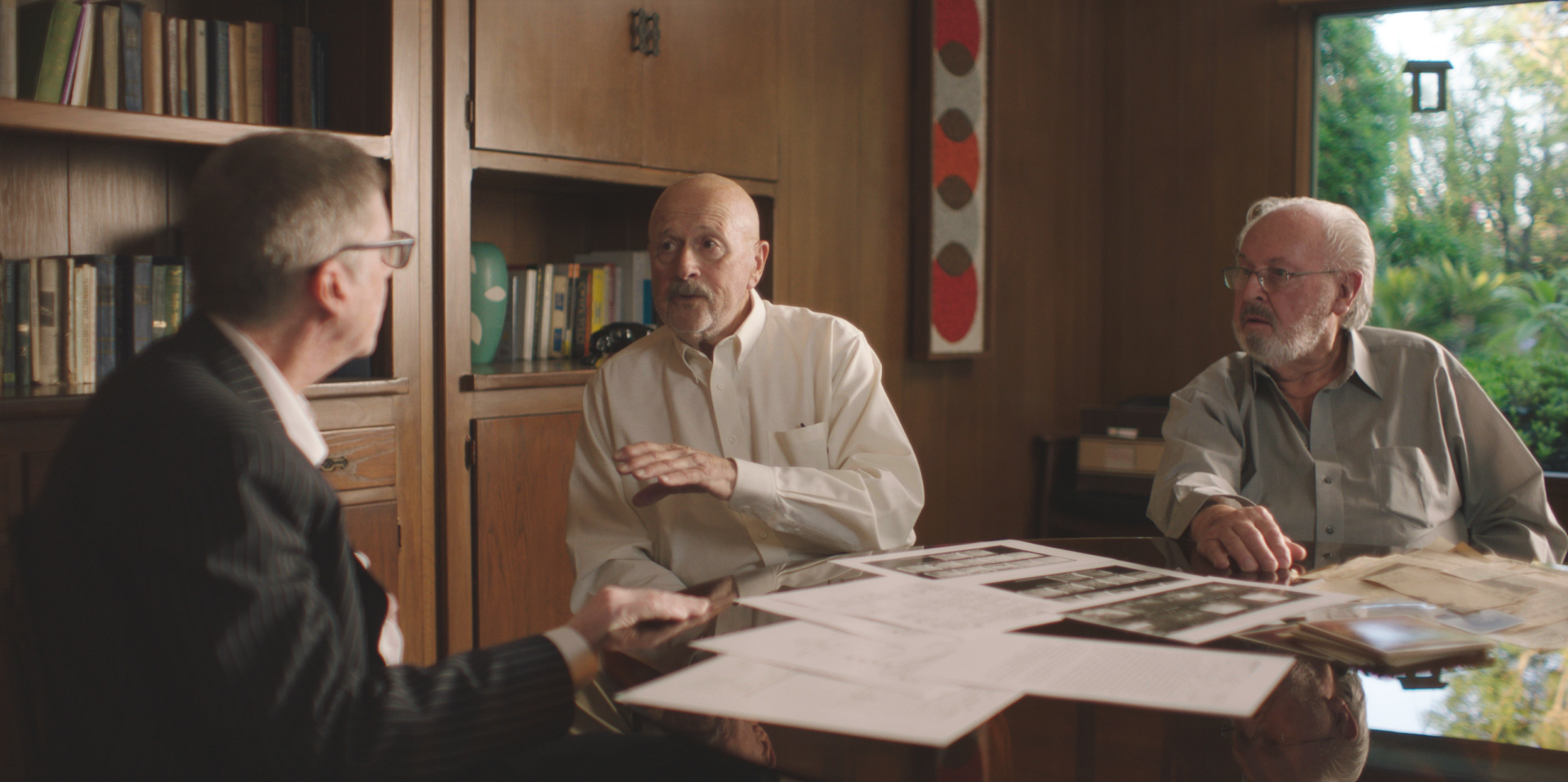 three men sit around a table looking at files in a still from the hillside stranger true crime doc