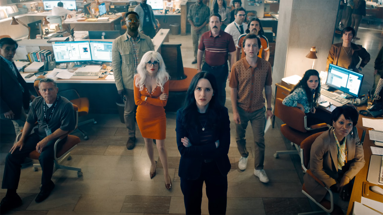 Cat Grant, Lois Lane, Steve Lombard, and Jimmy Olsen looking at an off-camera screen in The Daily Planet's newsroom in Superman