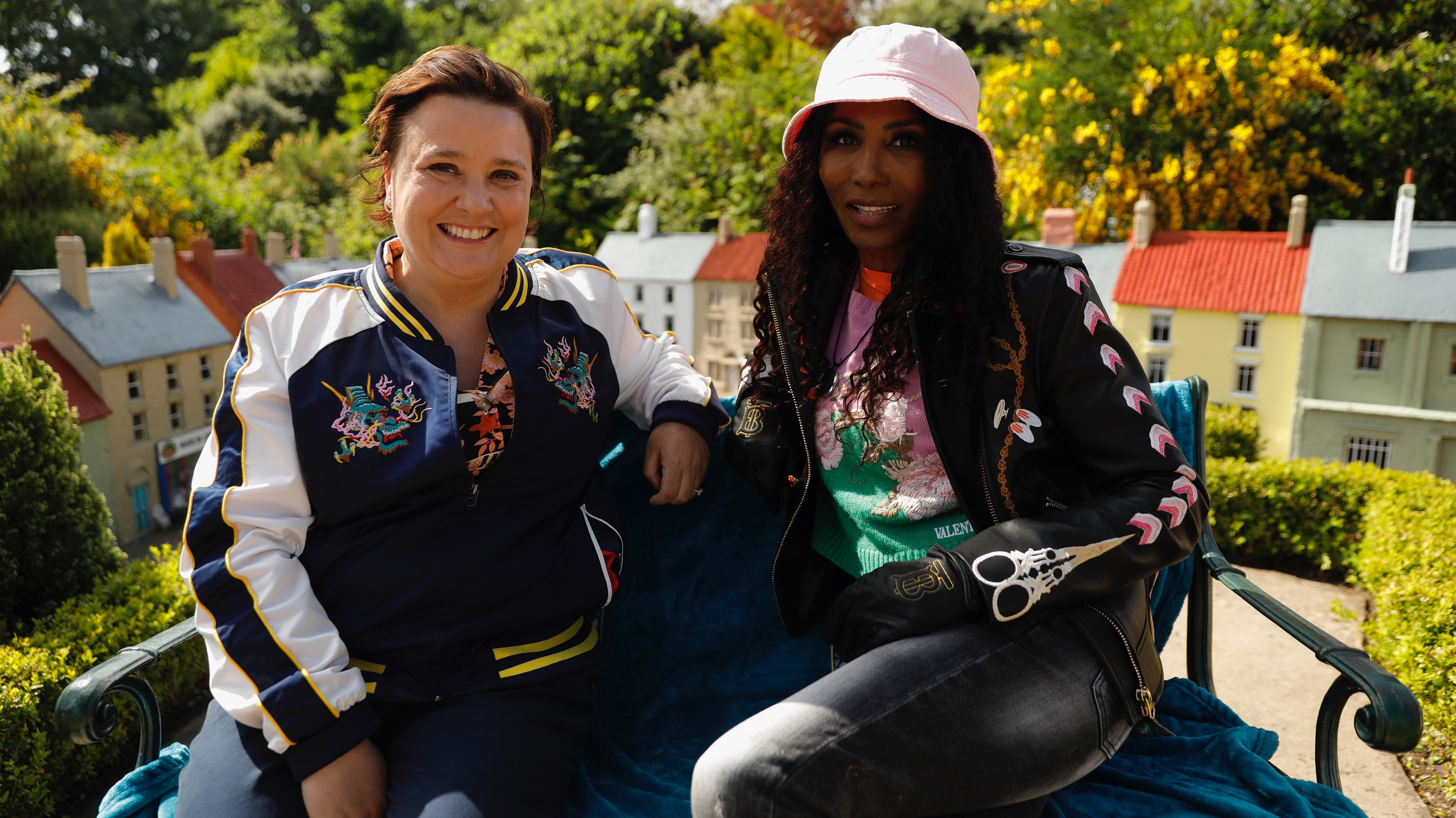 Susan and Sinitta sitting on a bench in a model village