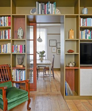 library with mustard book shelves and green chair looking through to dining room with white dining table