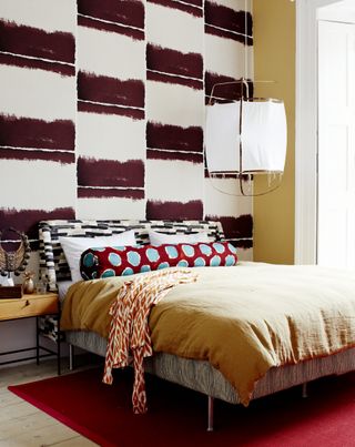 A bedroom with solid-toned bedding and ikat printed wallpaper