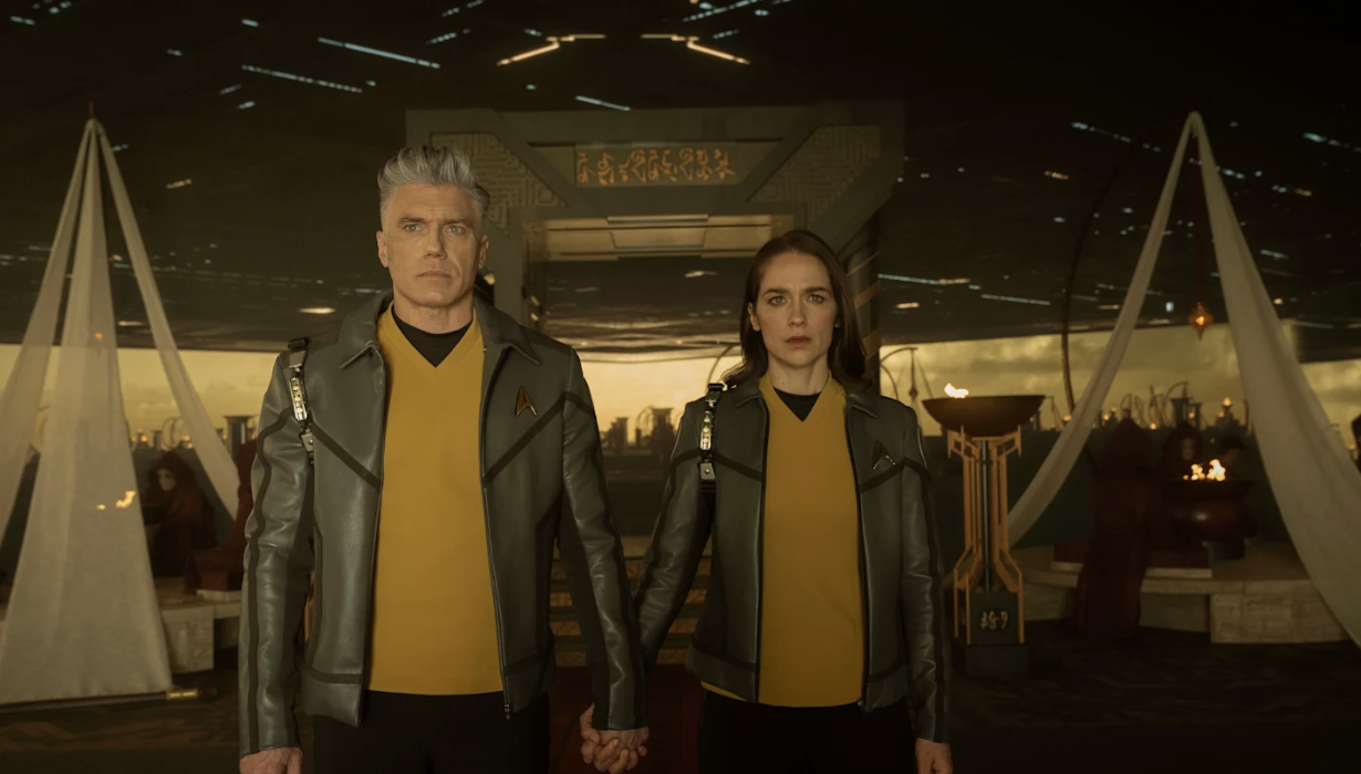 A man and a woman wearing gold uniforms link hands