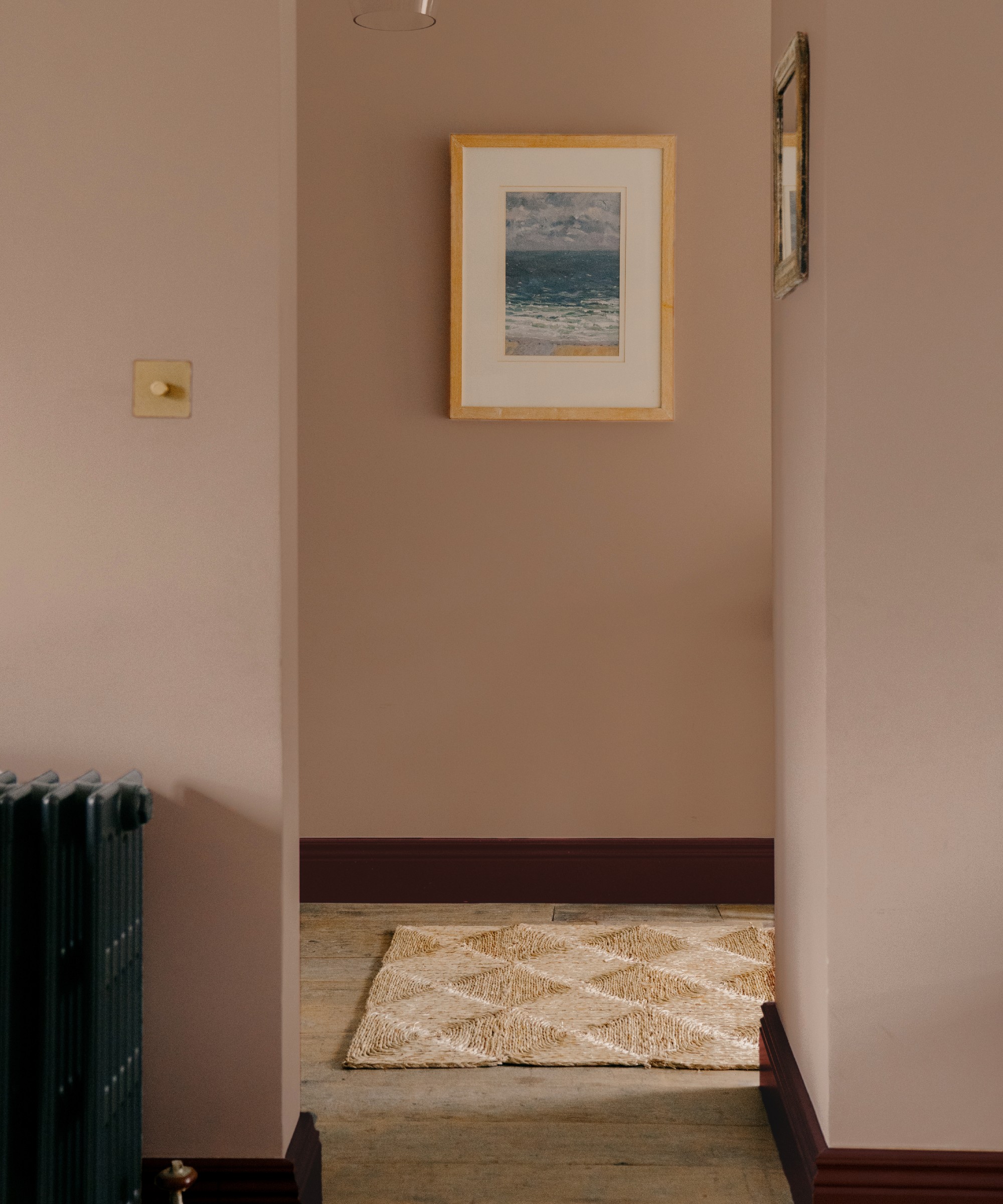 A pink hallway painted in COAT's Sybil with contrasting dark red skirting boards in Smith & The Devil