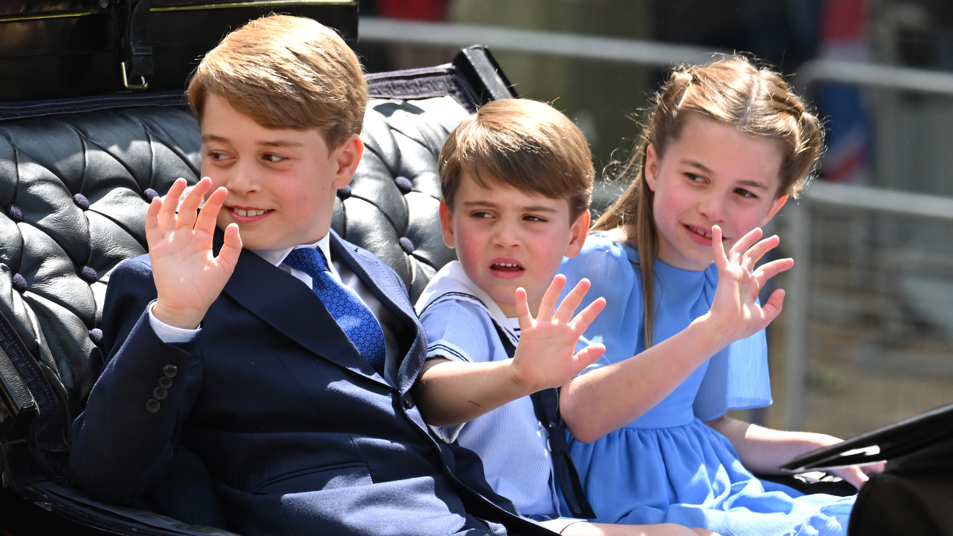 Prince George, Prince Louis and Princess Charlotte wearing blue outfits waving from a carriage at Trooping the Colour 2022