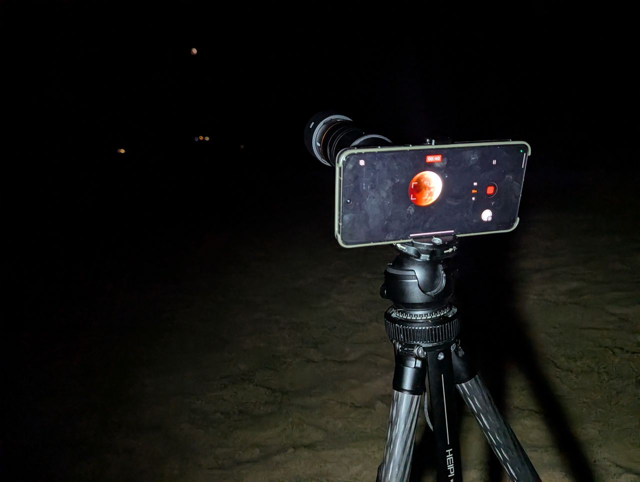 Oppo Find X9 Ultra phone with teleconverter lens mounted to a tripod on a beach at night during the 2026 lunar eclipse