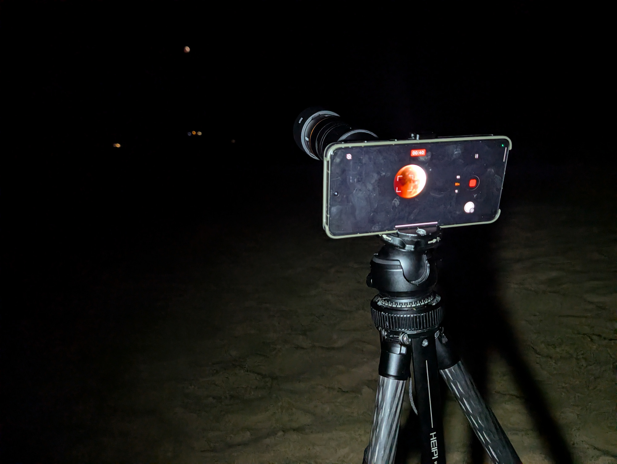Teléfono Oppo Find X9 Ultra con lente teleconversor montada en un trípode en una playa de noche durante el eclipse lunar de 2026