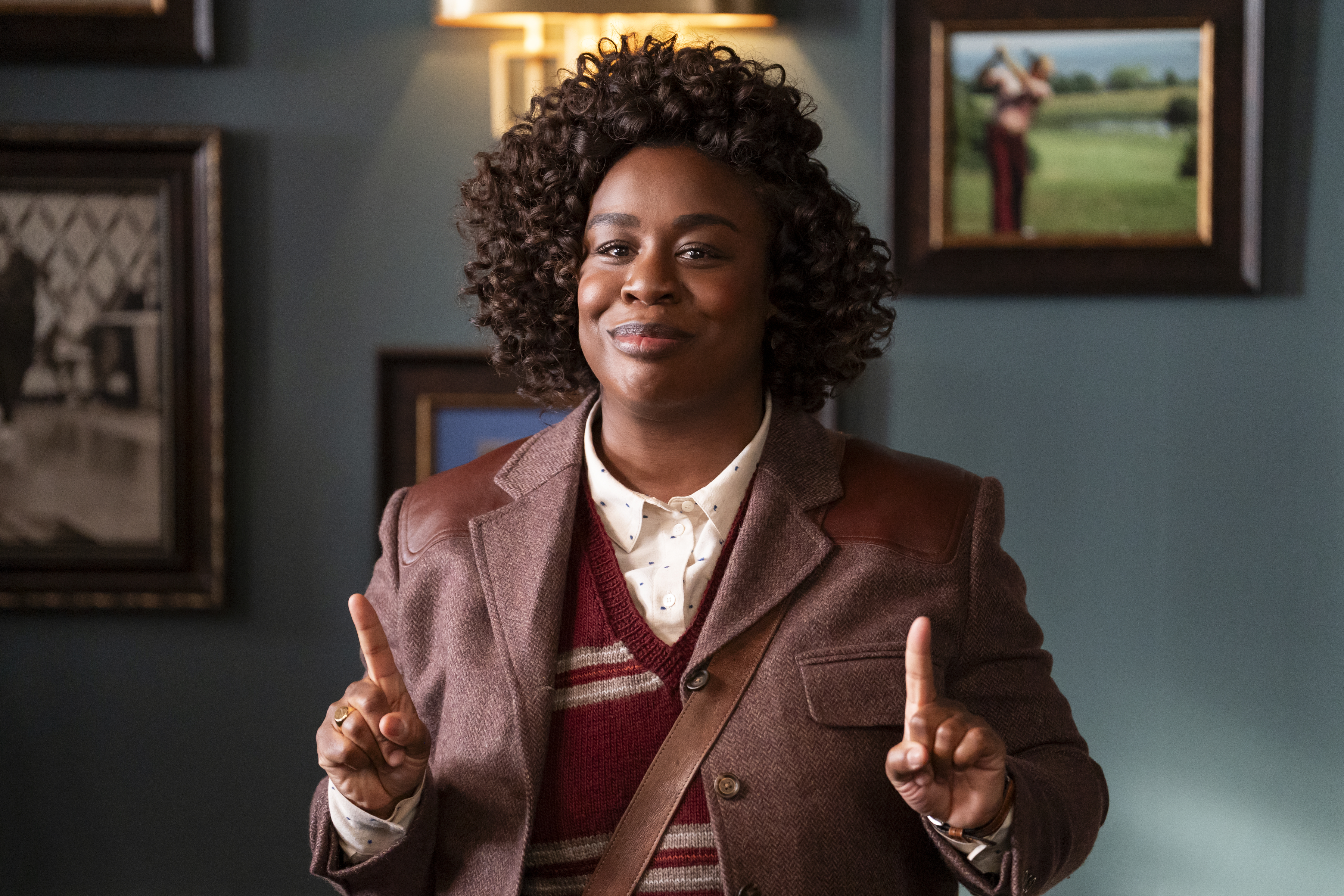 Uzo Aduba wears a brown leather jacket and sweater holding up two fingers smiling in a still from &#039;The Residence&#039;
