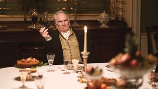 Rupert Vansittart in black jacket and yellow waistcoat at a dinner table as Charles Lawton in Gentleman Jack