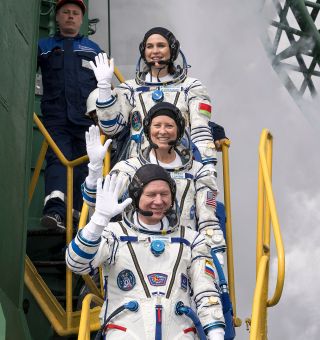 Soyuz MS-25 crewmates Oleg Novitsky, Tracy Dyson and Marina Vasilevskaya wave from the base of their Soyuz-2.1a rocket prior to boarding their spacecraft for launch.