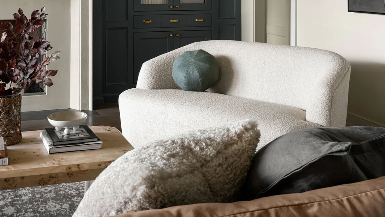 White boucle settee styled with a muted blue ball pillow in a cozy living room that features a burlwood coffee table and collected objects