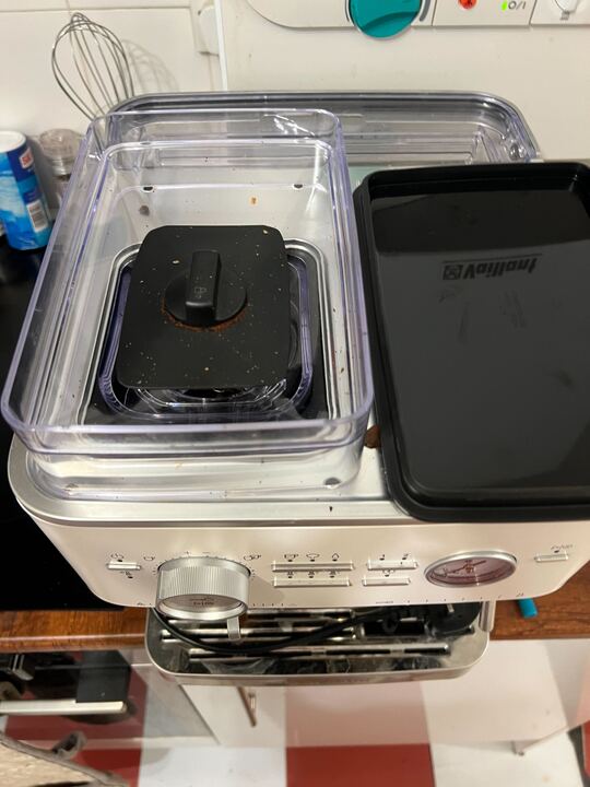 Image of the top of a coffee machine with the grinder open and coffee grinds still in it.