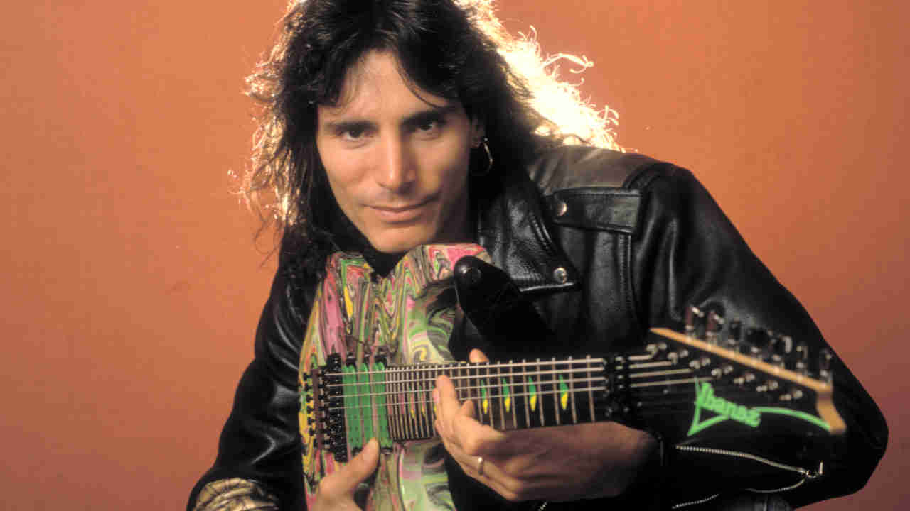 Steve Vai posing for a photograph while holding a guitar in 1990