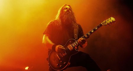 Lamb of God's Mark Morton performs live on a stage lit in yellow and orange. He plays his new Les Paul Modern Quilt