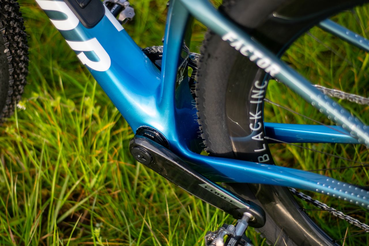A blue Factor Sarana gravel bike in a grassy field with a hedge in the background
