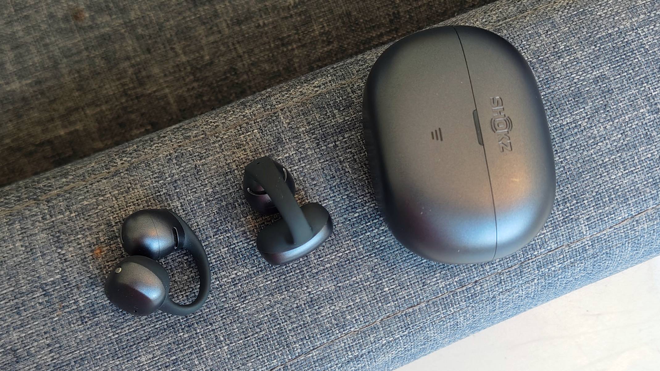 The Shokz OpenDots Air case and earbuds on the arm of a sofa.
