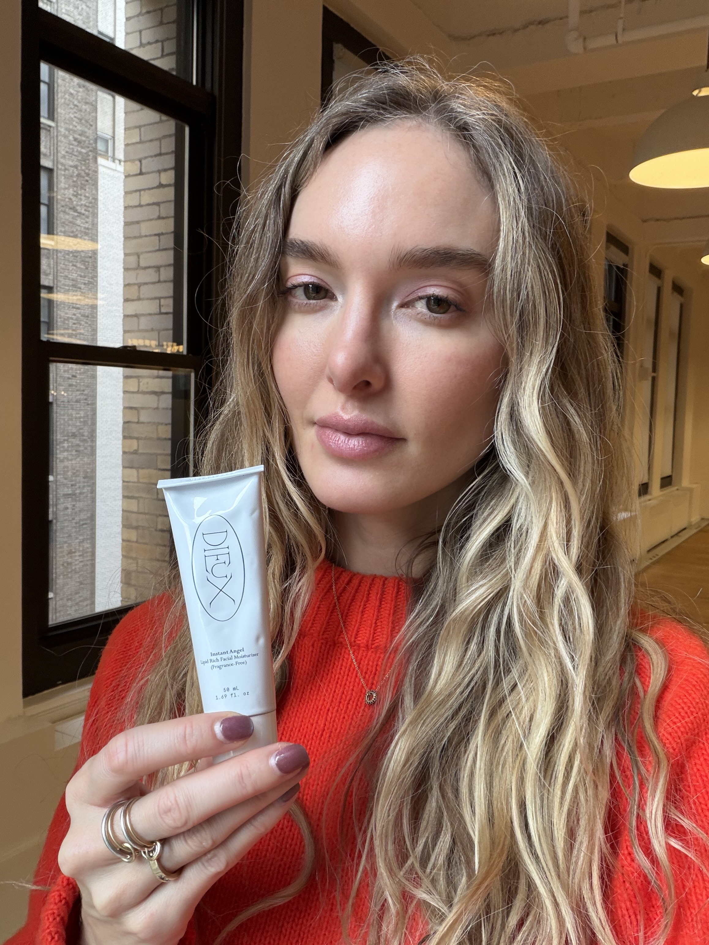 Hannah Baxter in a red sweater holding a white bottle of moisturizer