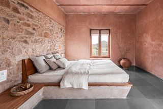 Bedroom with a double bed, white linen, a pot in the corner. Stone walls.