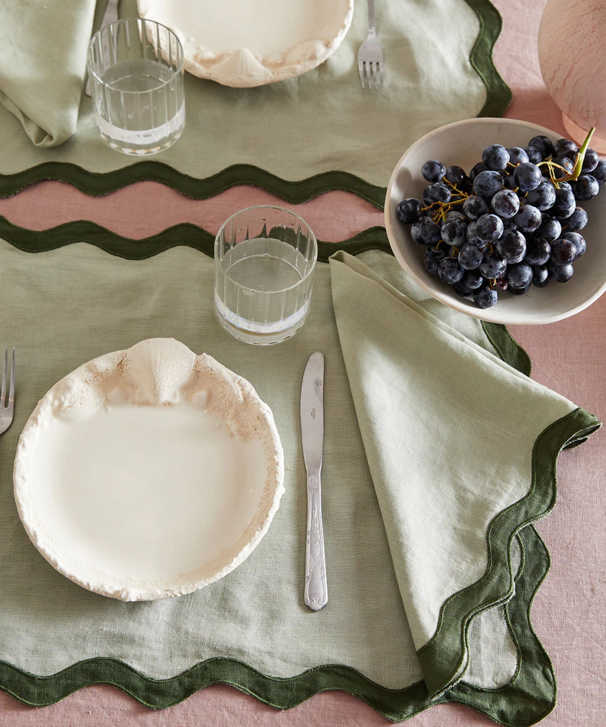 Pale pink tablecloth layered with pale green scalloped napkins with a dark green trim