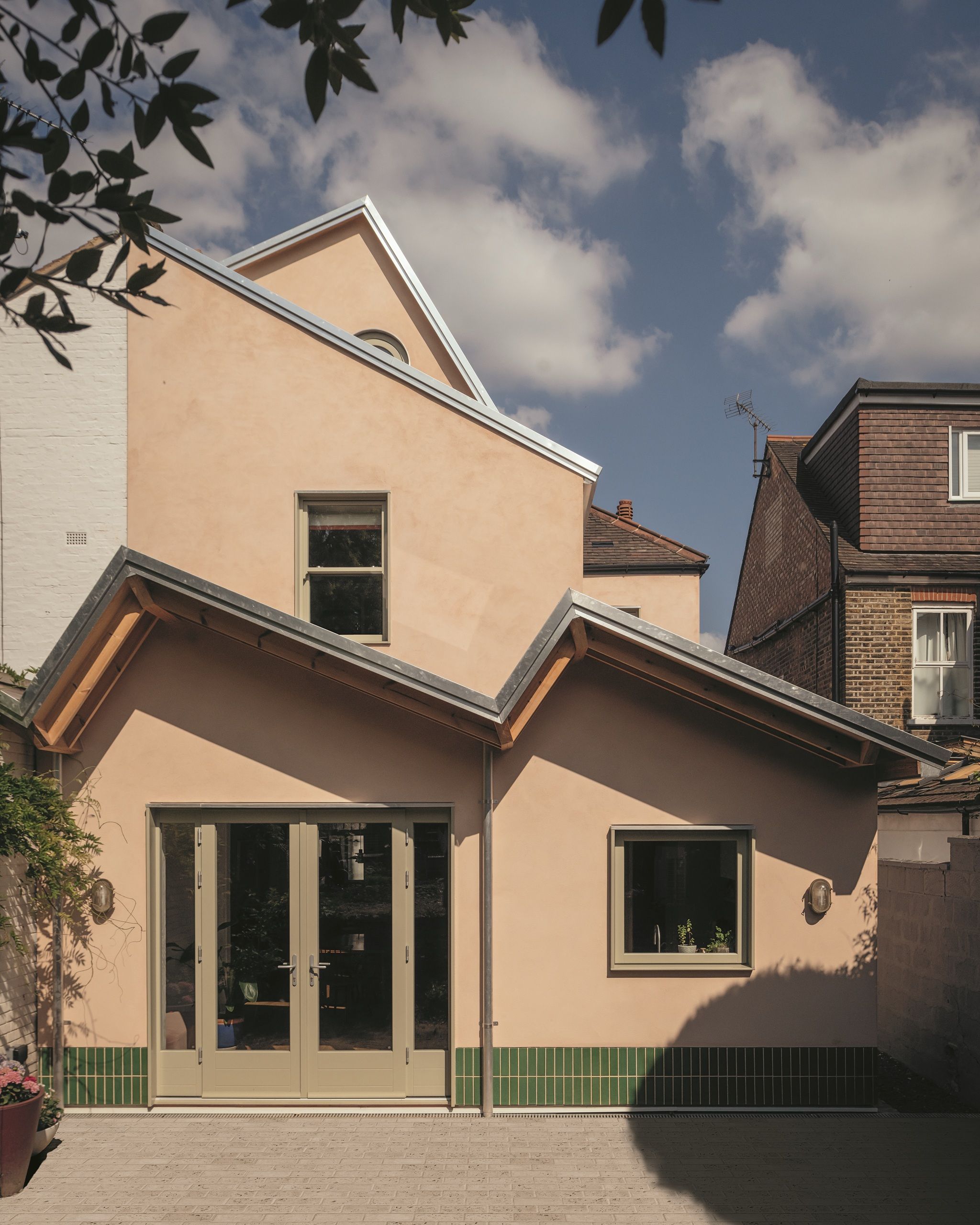 modern extension with sawtooth roof, green tiled skirting, and plaster pink exterior finish with french doors
