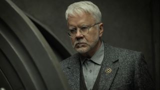 Tim Robbins stands with a stern look of disapproval on his face in Silo S2 E3 - "Solo".