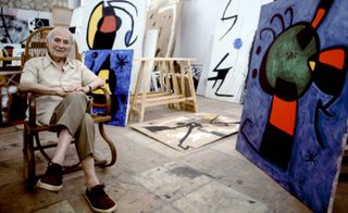 Joan Miró sat in front of his paintings