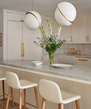 neutral kitchen with marble worktops, cream barstools and statement pendants