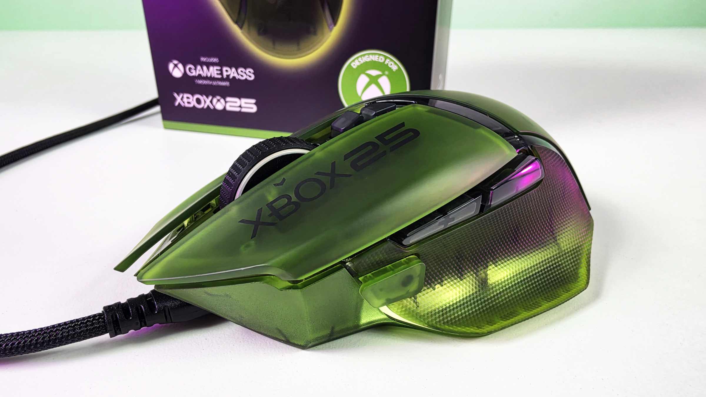 Wired side view of the Razer Basilisk V3 Pro 35K Xbox 25th Anniversary mouse with translucent green shell, glowing underglow, and box behind.