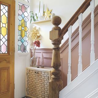 White painted hallway with pink panelling up the stairs and stained glass windows in the wooden door