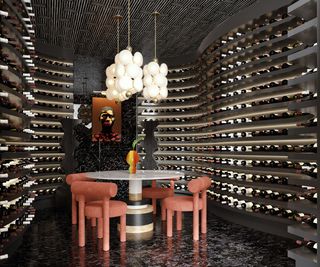 A wine cellar with curved wine racks along the walls and a round table with pink chairs below pendant lights.