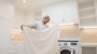 Senior man folding sheets in laundry room